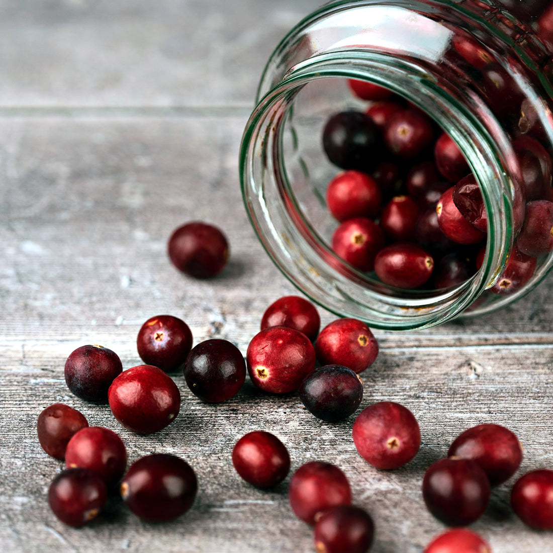 Fresh cranberries spilling from a tipped glass jar onto a wooden table