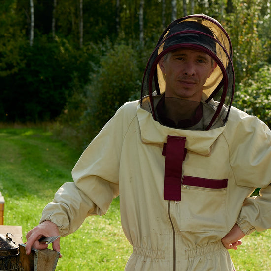 Beekeeper Andis in a protective suit and veil, standing in a meadow by the forest