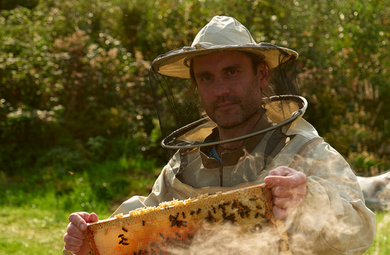 Founder Erlands in a beekeeping veil holding a honeycomb frame with bees