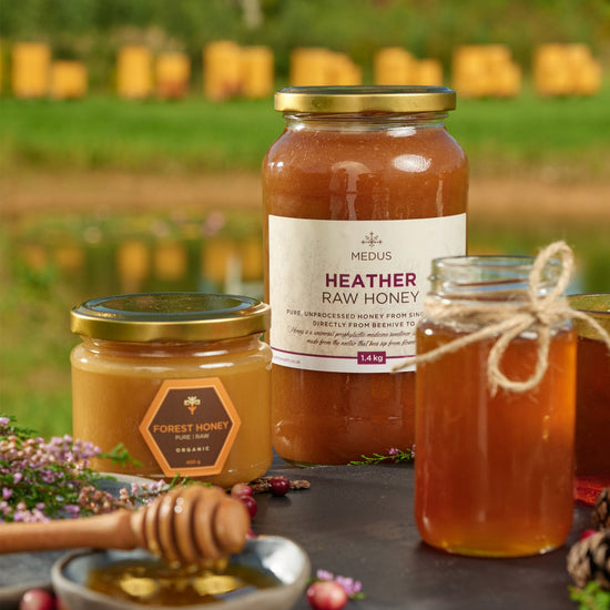 1.4kg jar of Heather Raw Honey beside a Forest Honey jar and honey dipper, beehives behind